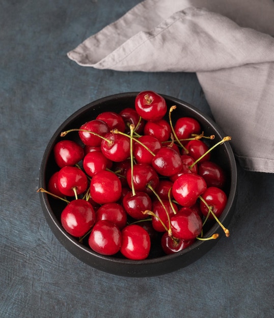 Fresh cherries in a black bowl on a dark blue background with napkin Top view