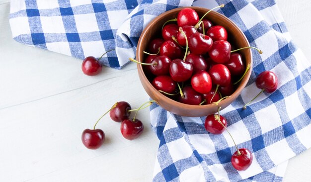 Photo fresh cherries in a clay bowl on the white table and a kitchen counter in a blue cage. top view