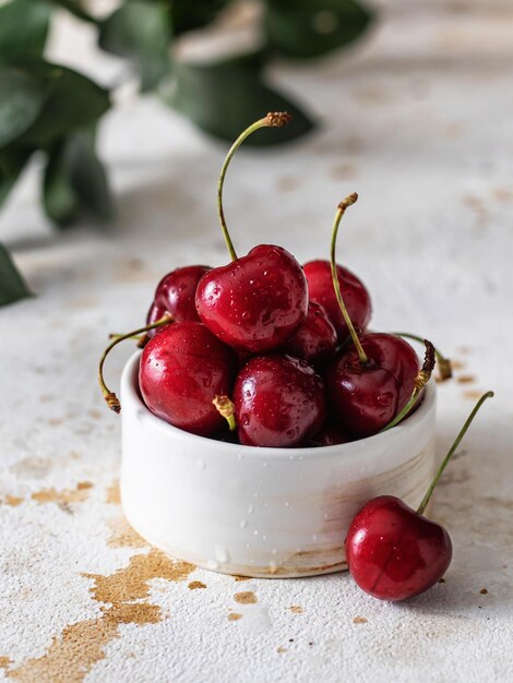 Fresh cherries close up in white ceramic bowl beautiful composition with greens on textured background