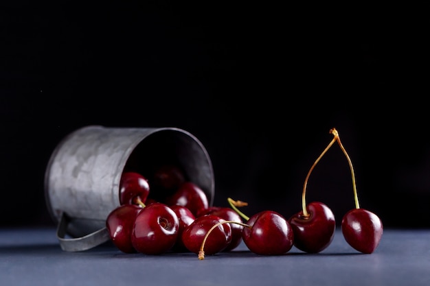 Fresh cherries in a metal mug on a black background