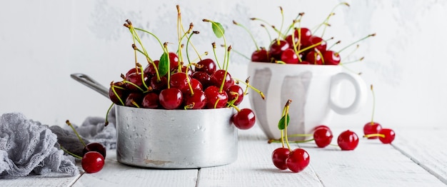 Fresh cherries in rustic aluminum saucepan on light wooden old background