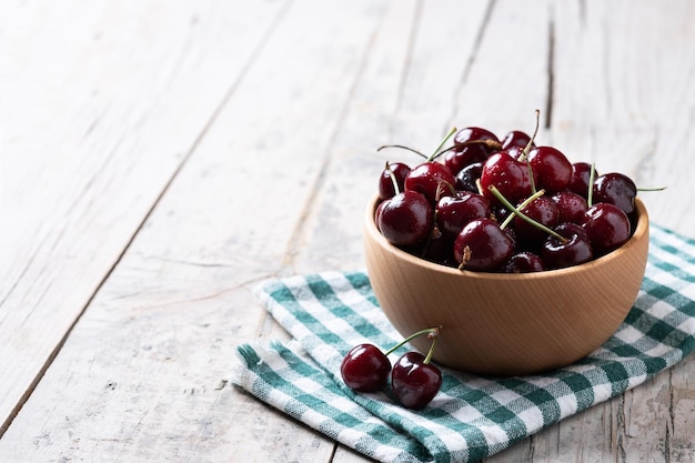 Fresh cherries with water drops in wooden bowl on white wooden table