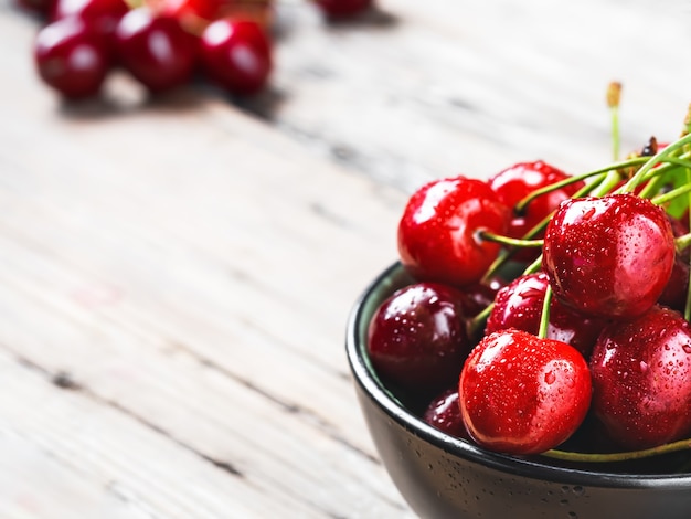 Fresh cherry berries with drops of water in a black bowl