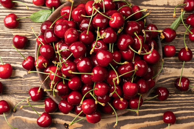 Fresh cherry on black plate on brown wooden background Top view, copy space, selective focus Red ripe sweet cherries on a table, vintage view