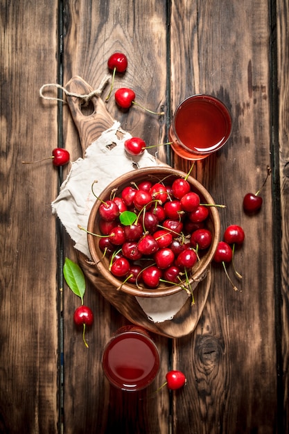 Fresh cherry and the juice in the glasses. On wooden background.