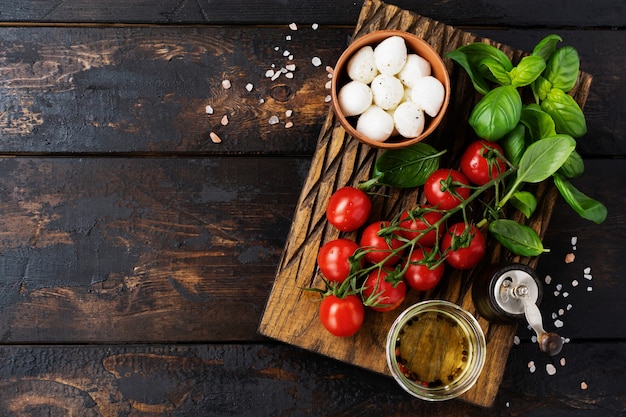 Fresh cherry tomatoes, basil leaves, mozzarella cheese and olive oil on old wooden background. Caprese salad ingredients. Selective focus.