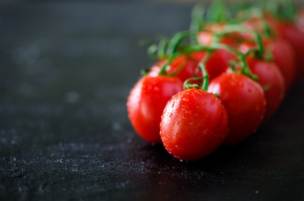 Fresh cherry tomatoes on black with basil, spices.