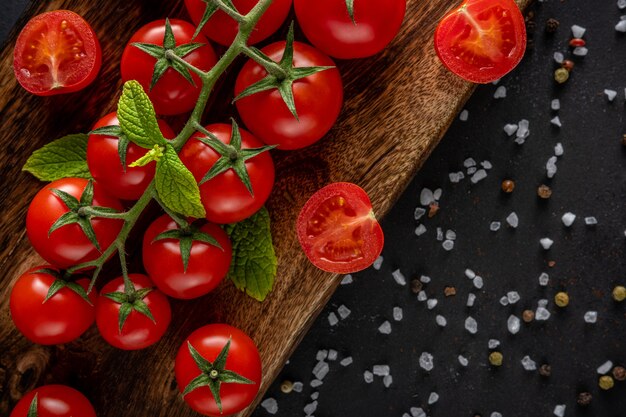 Fresh cherry tomatoes on a black with spices.