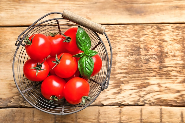 Fresh cherry tomatoes in metal basket on wooden table