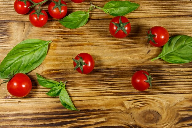Fresh cherry tomatoes with green basil leaves on a wooden table Top view