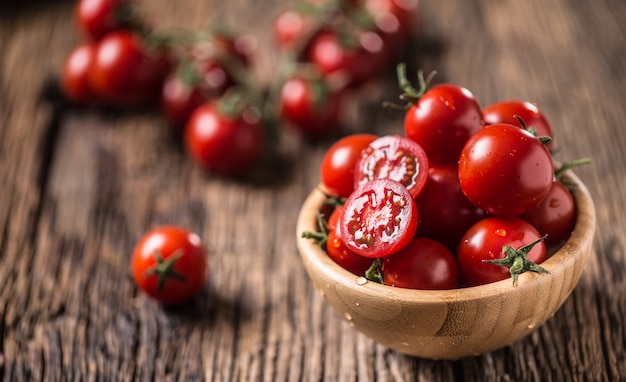 Fresh cherry tomatoes in wooden bowl on old oak table.