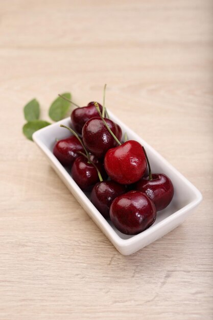 Photo fresh cherry in white bowl on wooden background