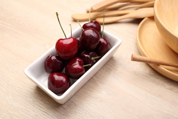 Photo fresh cherry in white bowl and wooden bowl on wooden background