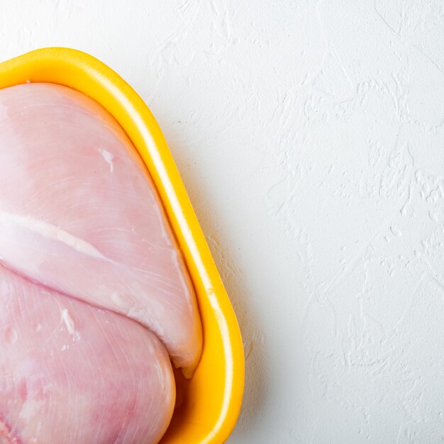 Fresh chicken breast meat in open tray, on white table