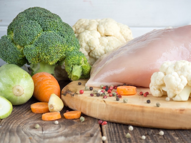 Fresh chicken breast and vegetables on rustic wooden background