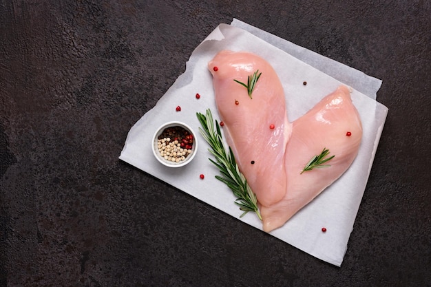 Fresh chicken breast with spices and herbs on black stone background Heart shaped chicken fillet Preparation for cooking