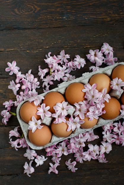 Foto uova marroni fresche del pollo in contenitore di cartone sulla tavola di legno. concetto di agricoltura biologica. alimento naturale sano. uova nel vassoio e fiori. moody easter