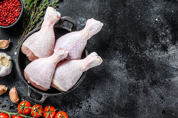 Fresh chicken drumsticks, legs with ingredients for cooking in a frying pan. Organic poultry meat. Black background.