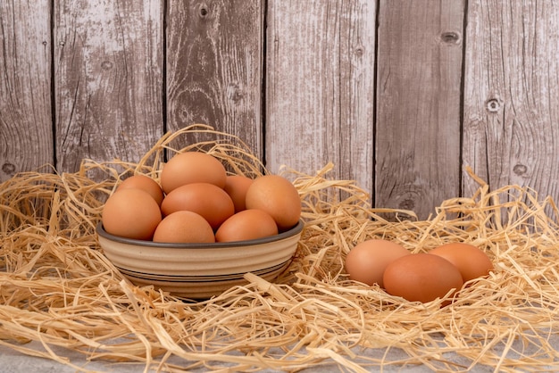 Fresh chicken eggs with brown shells in a bowl on a straw Rustic brown background