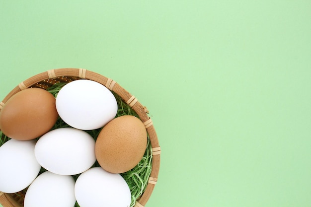 Fresh chicken eggs in wooden rattan wicker basket on green background. Natural healthy nutrition org