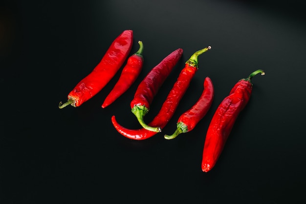 Fresh chili peppers of red color evenly arranged on a black background.