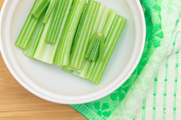 Fresh chopped celery sticks with water drops in white bowl