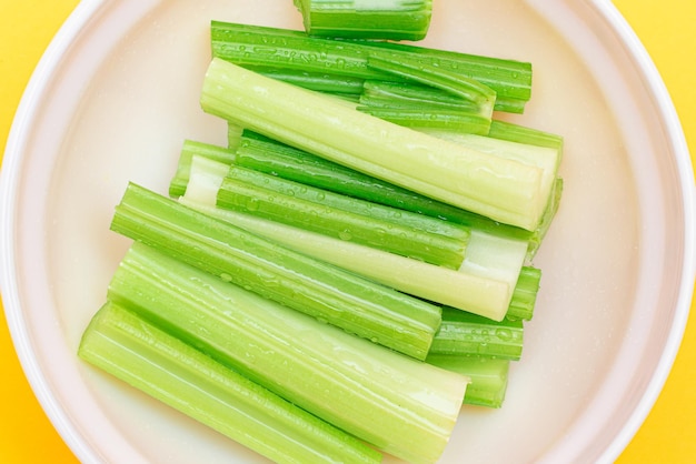 Fresh chopped celery sticks with water drops in white bowl