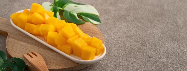 Photo fresh chopped diced mango cubes on gray table background with tropical leaf for eating