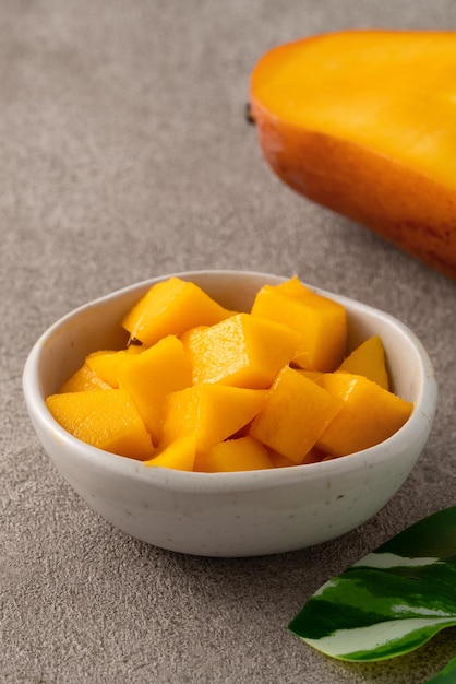 Photo fresh chopped diced mango cubes on gray table background with tropical leaf for eating