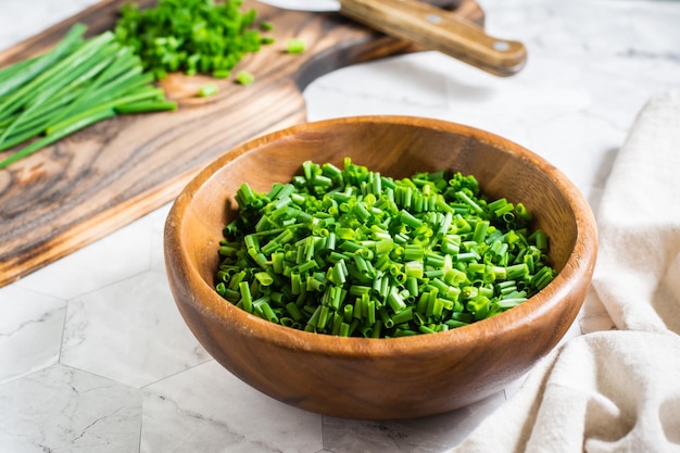 Fresh chopped green onions in a wooden bowl and a cutting board on the table Closeup