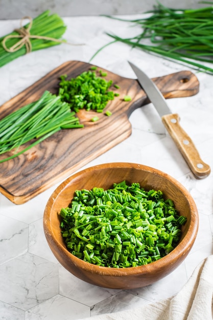 Fresh chopped green onions in a wooden bowl and a cutting board on the table Vertical view