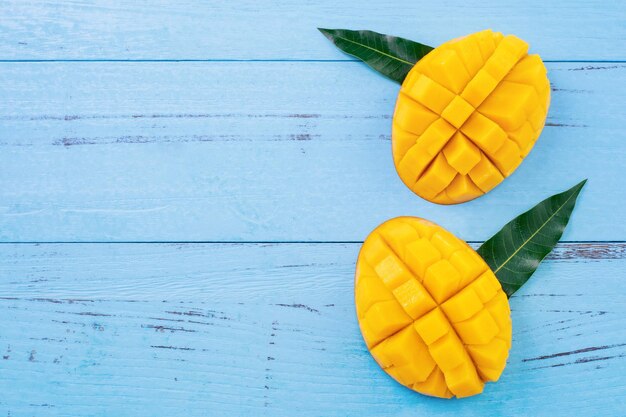 Fresh chopped mango with green leaves on bright blue color timber background Above Top view flat lay copy space close up Tropical fruit concept