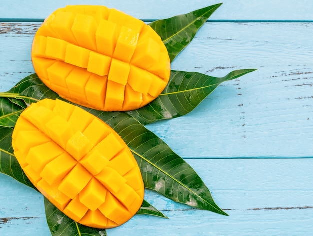 Fresh chopped mango with green leaves on bright blue color timber background