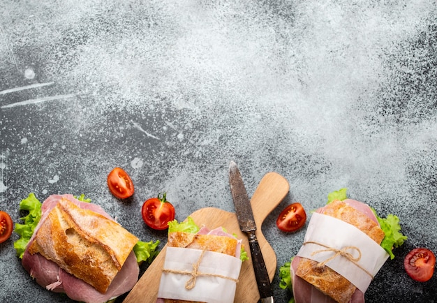 Fresh ciabatta sandwiches with ham, cheese, lettuce, tomatoes, stone concrete background, close-up, top view with space for text. Food template with making healthy sandwiches for snack or lunch