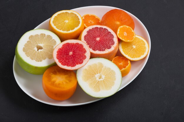 白い皿の上の新鮮な柑橘系の果物がクローズアップ、暗い背景