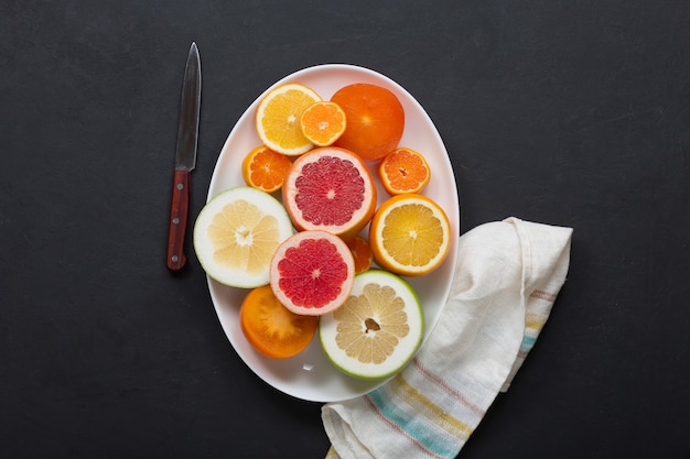白い皿の上の新鮮な柑橘系の果物がクローズアップ、暗い背景