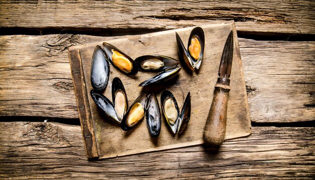 Fresh clams on a wooden Board with knife. On wooden background. Top view