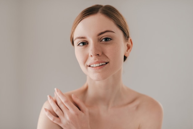 Fresh and clean. Portrait of gorgeous young woman with freckles on face smiling and looking at camera while standing against grey background