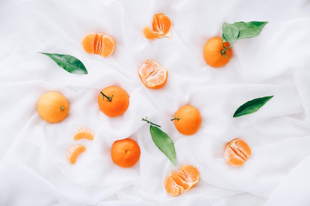 Fresh clementines with leaves on white fabric, top view