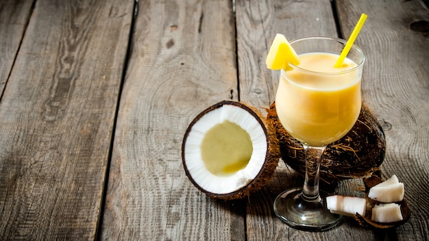 Fresh cocktail in a glass with coconut on wooden table. Free space for text.