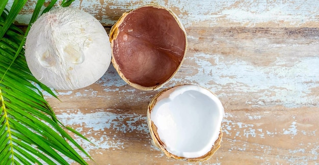 Fresh coconut with husks cut in half revealing white coconut\
flesh and coconut leaves on woodden