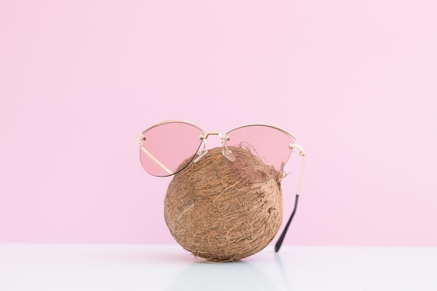 Fresh coconut with sunglasses on color background