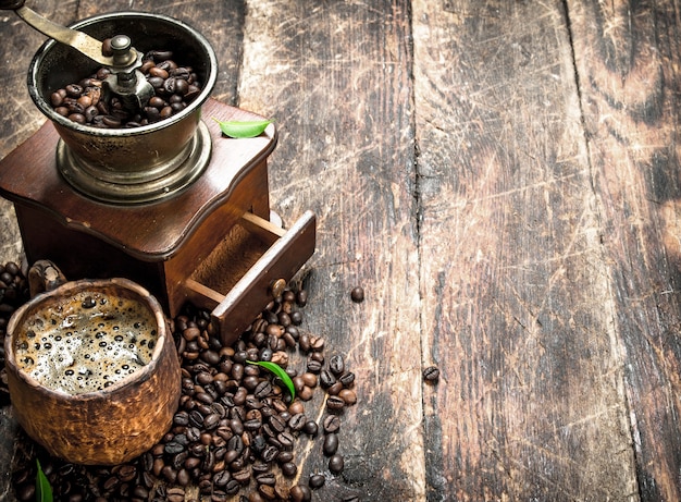 Fresh coffee in a clay mug with an old coffee grinder. On a wooden background.