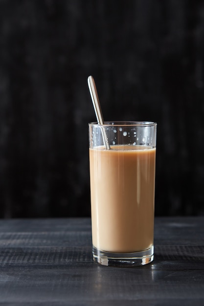 Caffè fresco con latte in un bicchiere con un cucchiaio di metallo su un tavolo di legno nero con spazio per le copie.