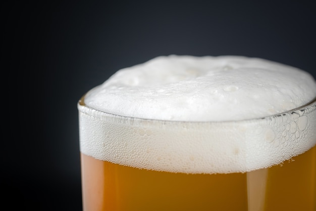 Fresh and cold glass craft beer with white foam on top.