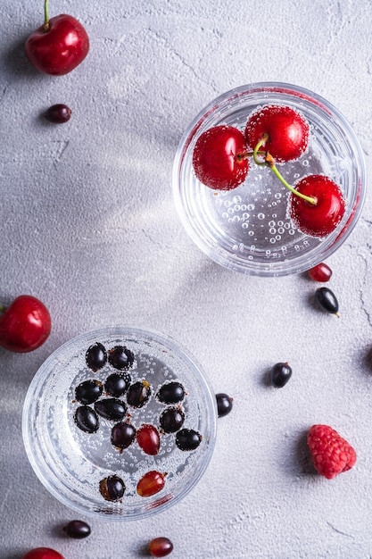 Fresh cold sparkling water drink with berries in two transparent glass on stone concrete