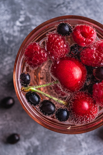Свежий холодный газированный напиток с вишней, малиной и ягодами смородины в красном граненом стекле