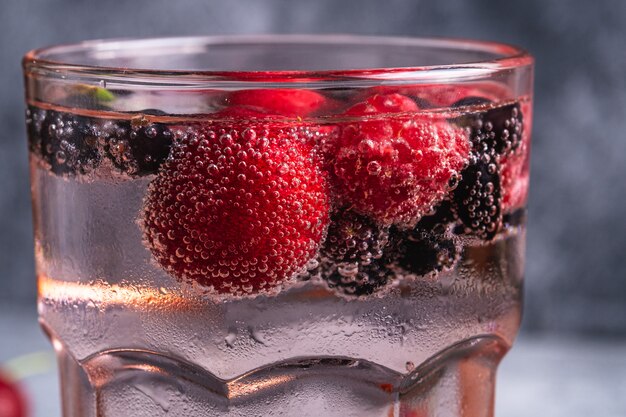 赤いファセットグラスにチェリー、ラズベリー、スグリの果実が入った新鮮な冷たい炭酸水ドリンク