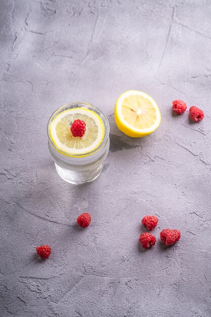 Fresh cold sparkling water drink with lemon, raspberry fruits in glass