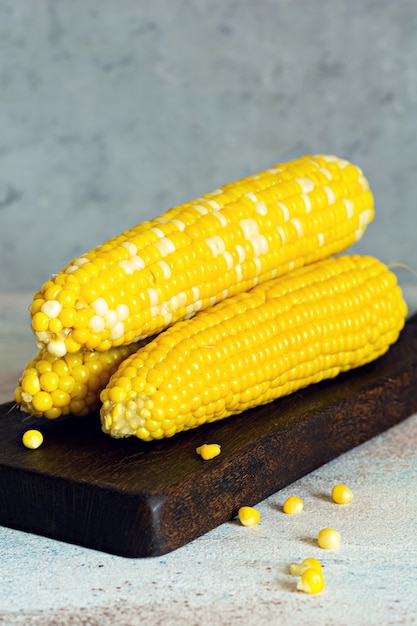 Fresh cooked (boiled) corn on a wooden board on a gray (blue) background. Ripe corn.